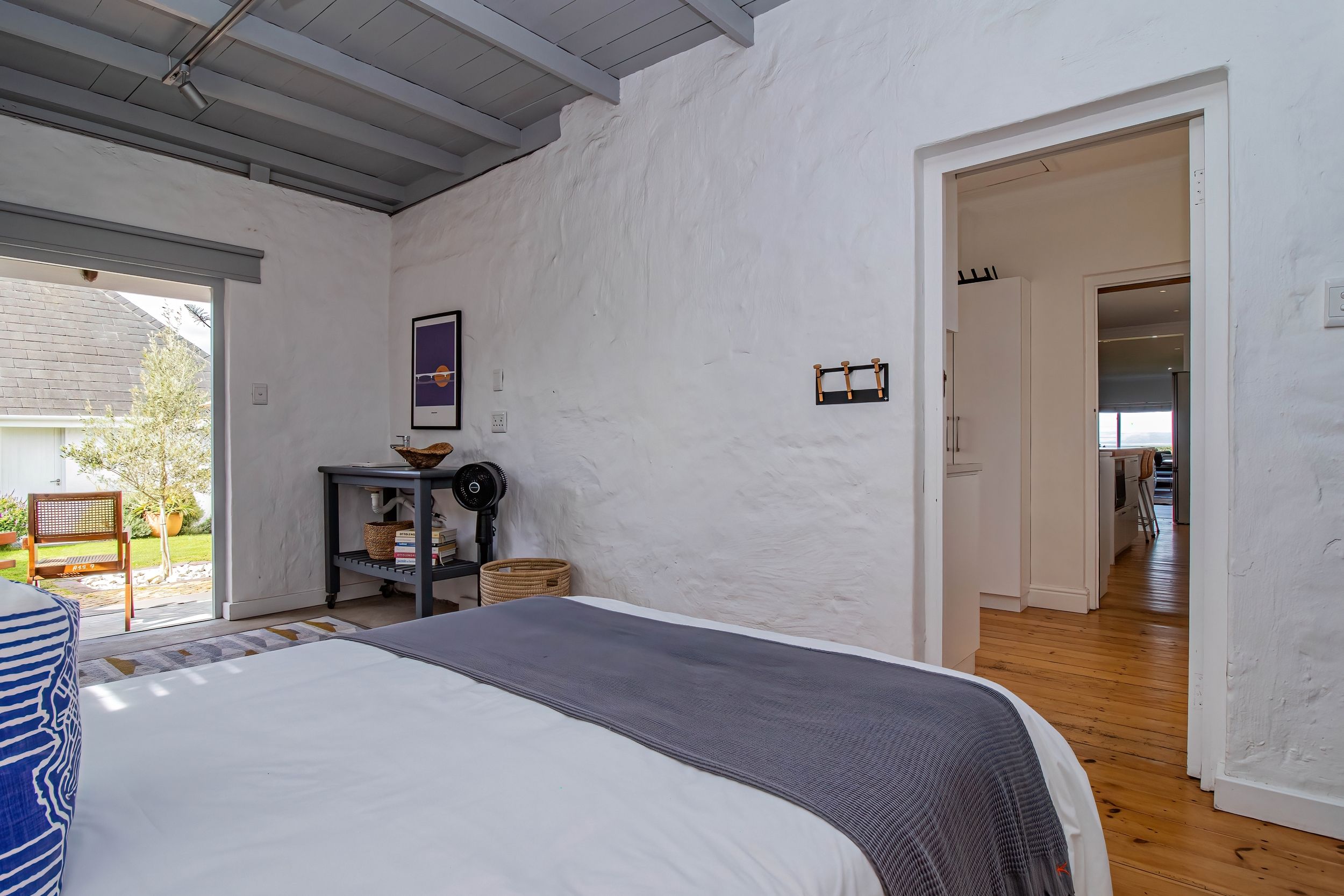A bedroom with a bed, a small table with a basket, a wall-mounted picture, and a door leading to another room.