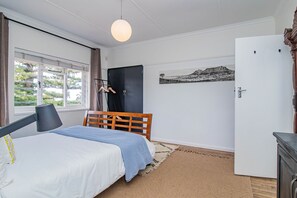 A bedroom with a bed, a wardrobe, a desk, and a window with a view of greenery. - Fairview Hermanus | Ocean View Home, Sleeps 8 (Hermanus)