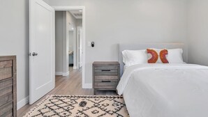Une chambre à coucher avec un lit, une table de chevet, une commode, une porte et un couloir.
