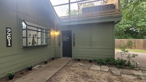 A house with a green exterior, a number '261' on the wall, a window with a view of plants, and a door with a 'welcome' sign. - Texas Evergreen Oasis WACO/Silos/Baylor: Pool, Spa, PingPong, Pets on 1/3 acre (Waco)