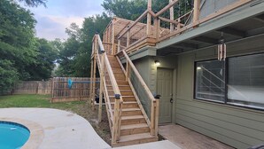 A house with a wooden staircase leading to a deck, a swimming pool, and a green door. - Texas Evergreen Oasis WACO/Silos/Baylor: Pool, Spa, PingPong, Pets on 1/3 acre (Waco)