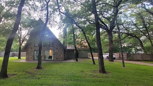 A modern house with a stone exterior, surrounded by a well-maintained lawn and tall trees. - Texas Evergreen Oasis WACO/Silos/Baylor: Pool, Spa, PingPong, Pets on 1/3 acre (Waco)