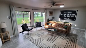 A living room with a leather sofa, a coffee table, and a view through large sliding glass doors to a backyard. - Texas Evergreen Oasis WACO/Silos/Baylor: Pool, Spa, PingPong, Pets on 1/3 acre (Waco)