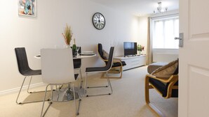Una sala de estar moderna con comedor, que incluye un sofá blanco, una silla negra, una mesa blanca y un reloj en la pared.