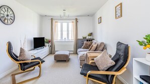 Una sala de estar moderna con un sofá, dos sillones, un televisor y una estantería.