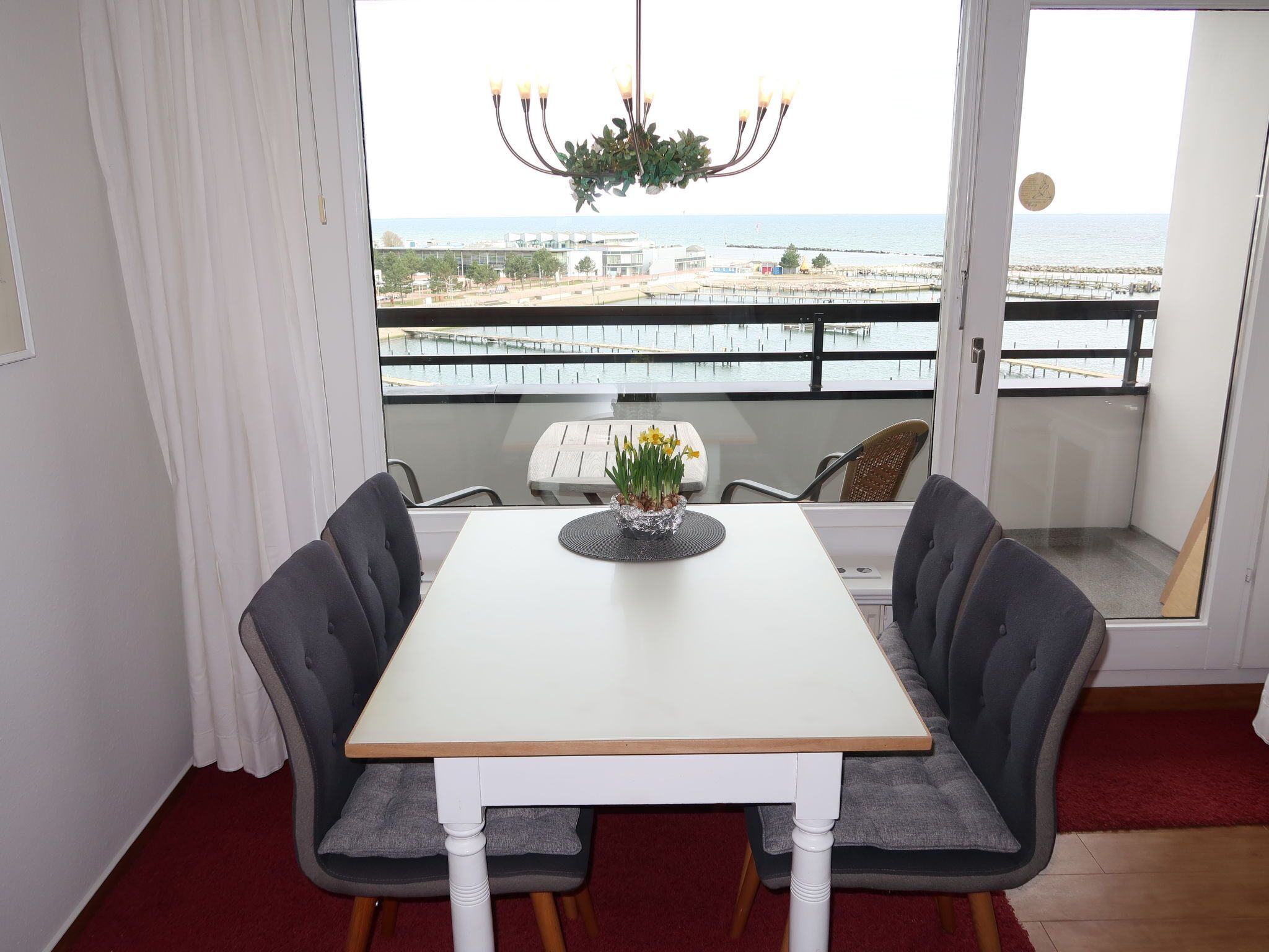 A dining area with a table and chairs, a chandelier, and a view of the sea and buildings.