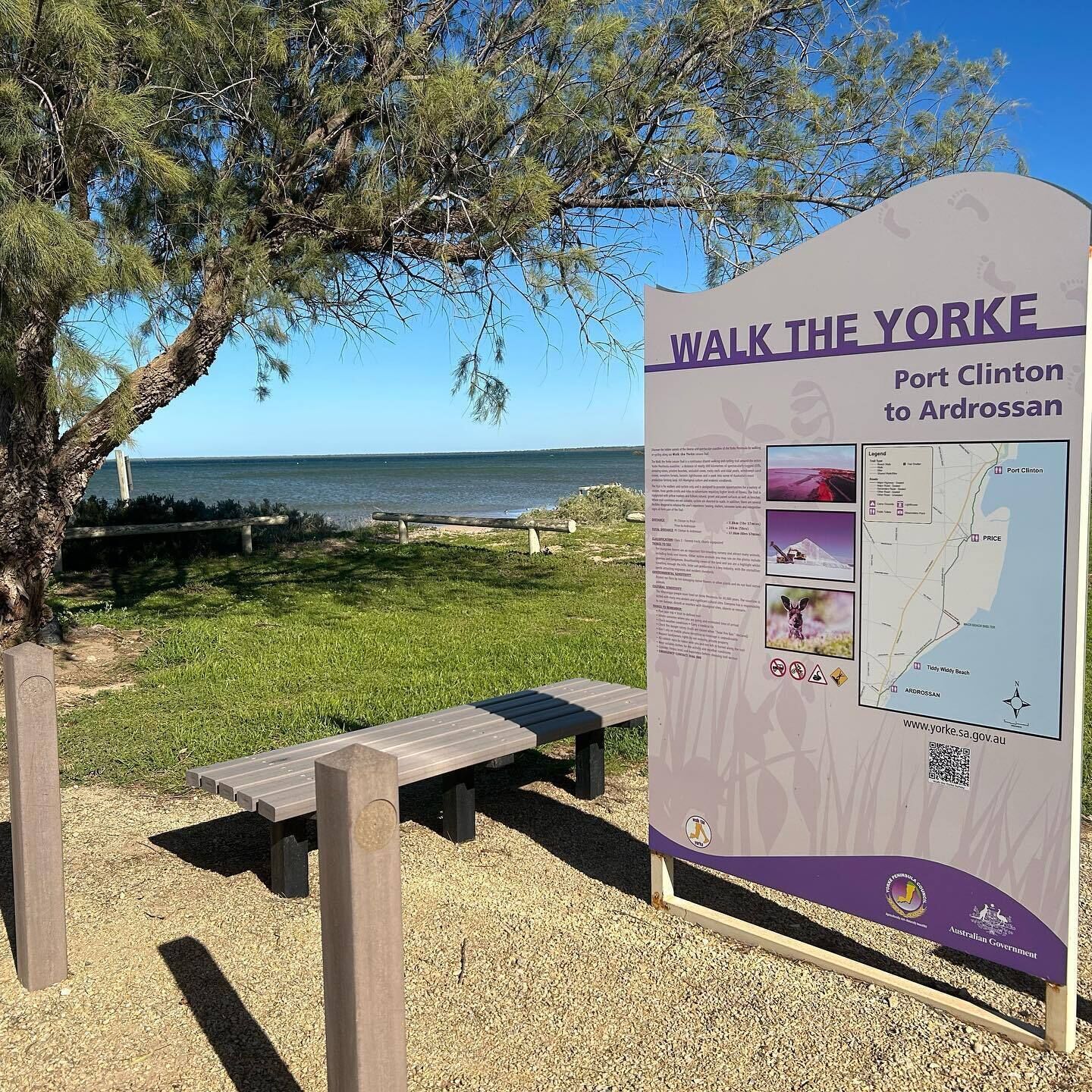 Placa de informação do parque com uma mesa para piquenique e vista para a praia.