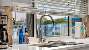 A modern kitchen with a stainless steel faucet, a coffee maker, and various cleaning supplies on the counter.