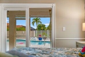 Une chambre d’hôtel avec vue sur une piscine, un balcon avec une balustrade et un lit recouvert d’une courtepointe à motifs.