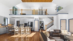 Amplia sala de estar con piso de madera, un sofá grande, una mesa de comedor con sillas y una cocina al fondo.