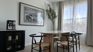 Ett modernt matområde med ett träbord och svarta stolar, ett inramat svartvitt fotografi av en häst, en kaffemaskin och en krukväxt.