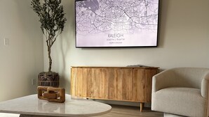 Ett modernt vardagsrum med ett soffbord i marmor, ett träskåp, en beige fåtölj och en väggmonterad karta över Raleigh, North Carolina.