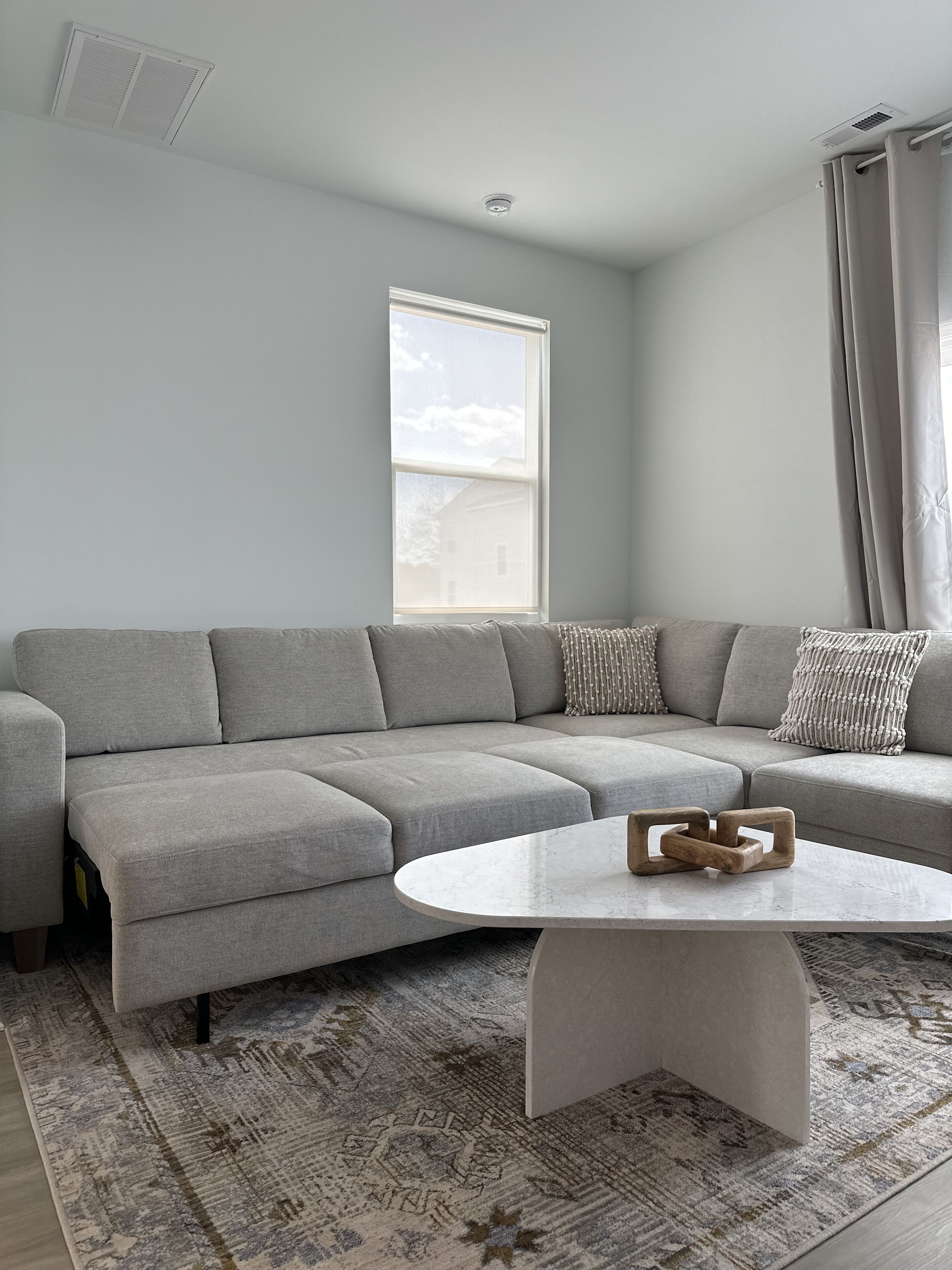 A modern living room with a grey sectional sofa, a round coffee table, and a patterned rug.