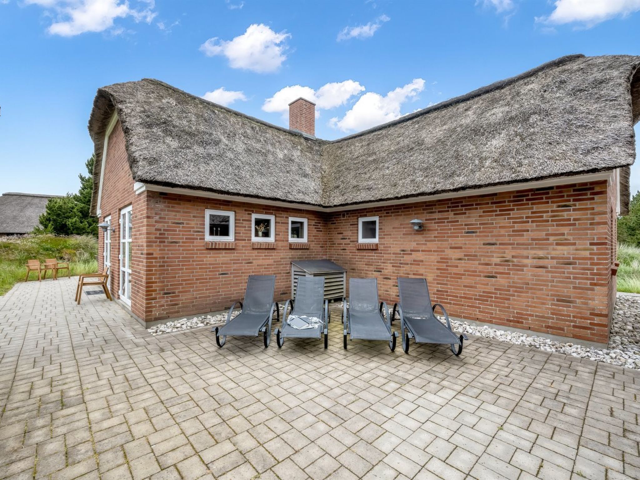 Un edificio in mattoni con tetto di paglia e un patio con poltrone da relax.