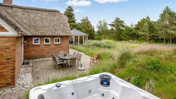 A cozy outdoor patio with a brick house, a thatched roof, and a hot tub.