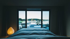 A hotel room with a large bed, a view of a pool and outdoor seating, and a lamp on the side table. - MOKU ISESHIMA (Shima)