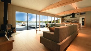 A spacious living area with a large window offering a view of the water, a cozy sofa, and a wooden ceiling structure. - MOKU ISESHIMA (Shima)
