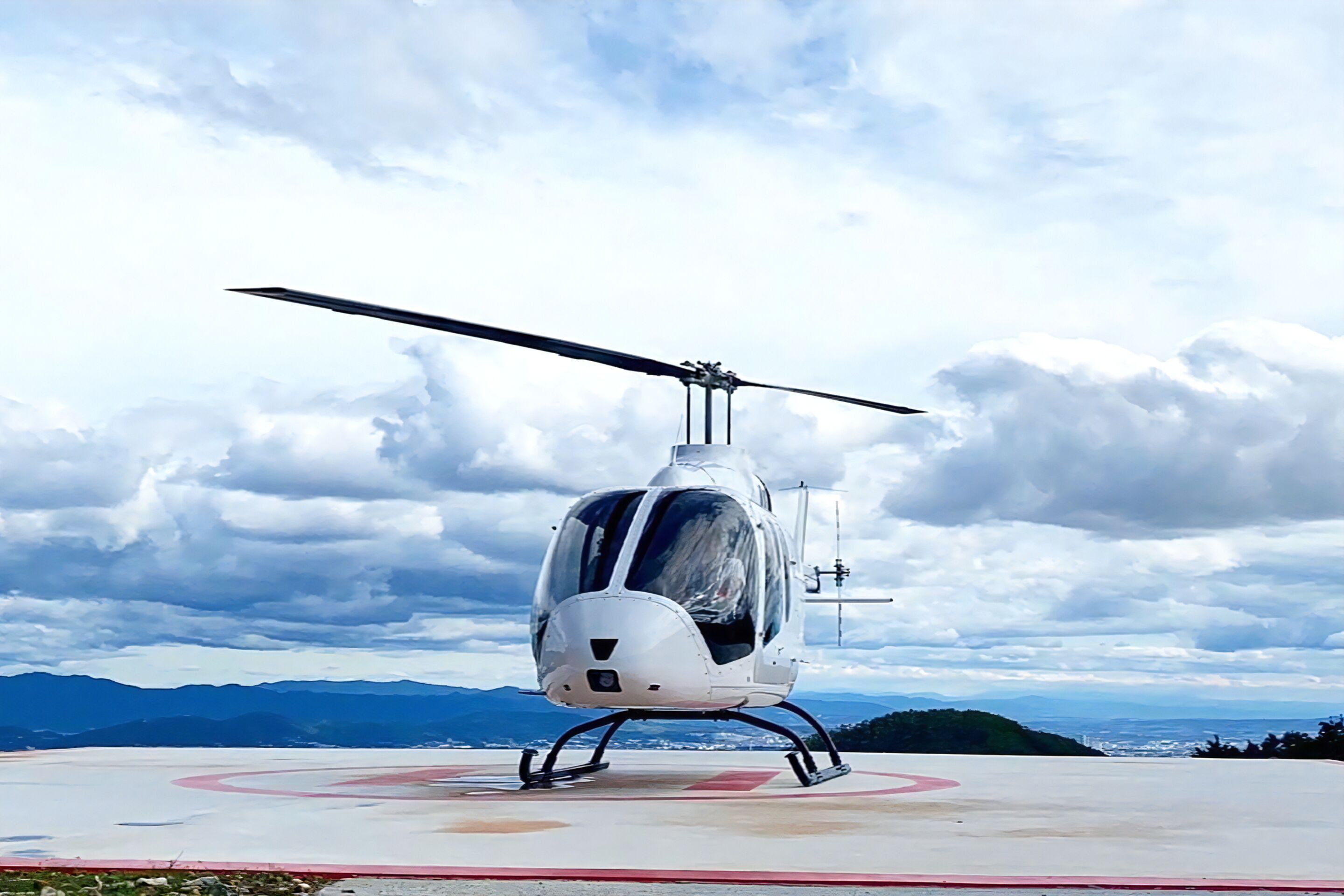 Um helicóptero estacionado em um heliponto, com uma paisagem montanhosa ao fundo.