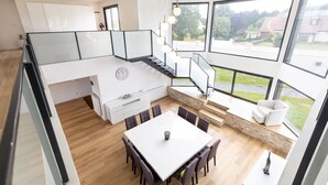 Een moderne keuken met een centraal eiland, een eethoek met tafel en stoelen, en grote ramen met uitzicht op de omgeving.