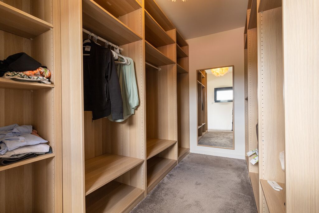 A walk-in closet with wooden shelving and hanging space, a carpeted floor, and a mirror reflecting the room.