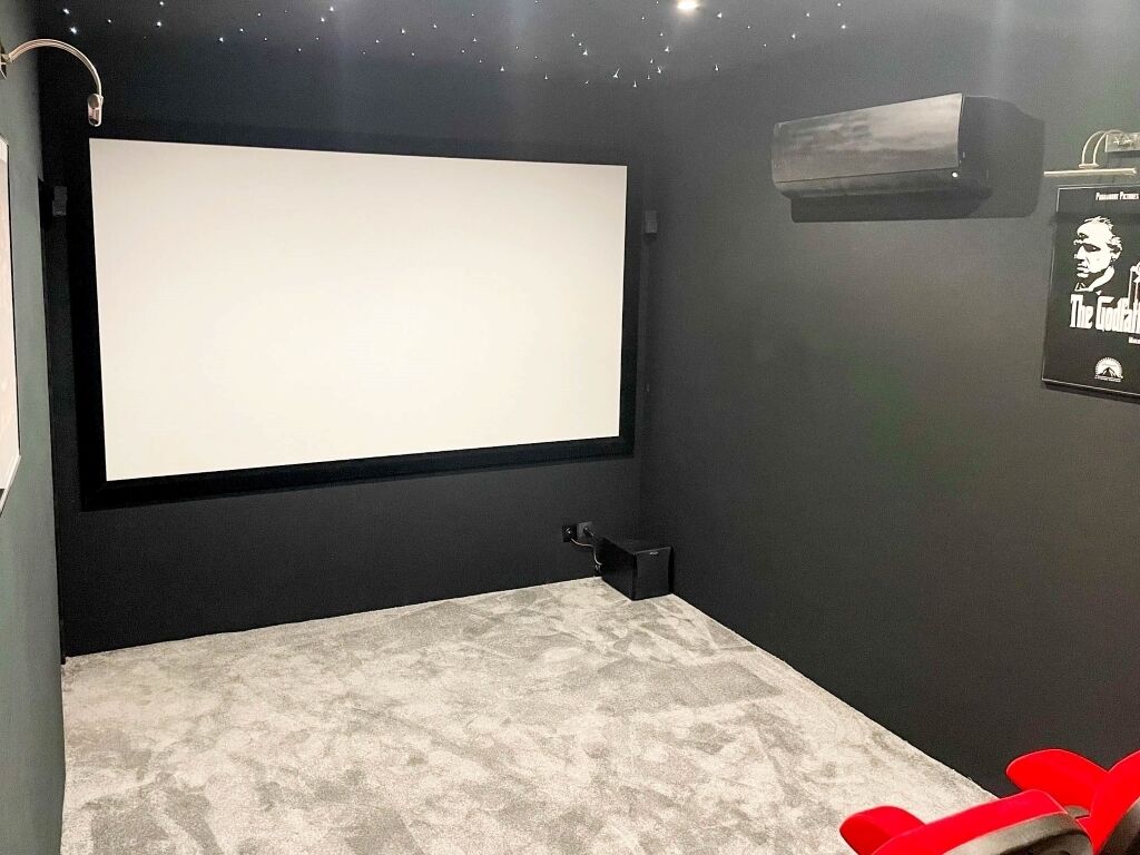 A room with a large white projection screen, a small black speaker, and a poster on the wall.