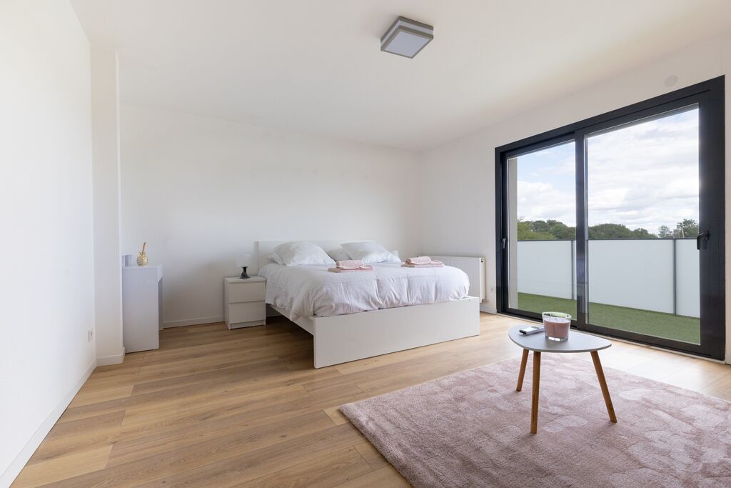 Ein modernes Schlafzimmer mit großem Fenster, einem Bett, einem Nachttisch und einem kleinen Tisch mit einem Glas.