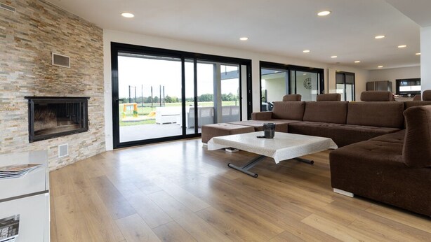 Een moderne woonkamer met een open haard, grote ramen en een bruine hoekbank.