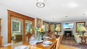 Une salle à manger avec une table en bois dressée pour six personnes, une cheminée et un téléviseur.