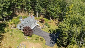 Une grande maison entourée d’une forêt dense, avec une allée et un espace extérieur aménagé pour s’asseoir.