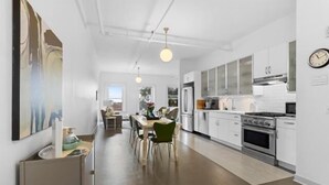 A modern kitchen with white cabinets, stainless steel appliances, and a dining area with a table and chairs. - Rockland Central Over Main, downtown living (Rockland)