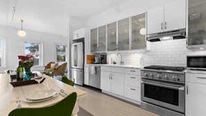 A modern kitchen with white cabinets, a stainless steel stove, and a dining area with a table set for two. - Rockland Central Over Main, downtown living (Rockland)