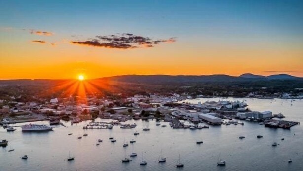 A coastal cityscape at sunset with numerous boats on the water and buildings in the background. - Rockland Central Over Main, downtown living (Rockland)