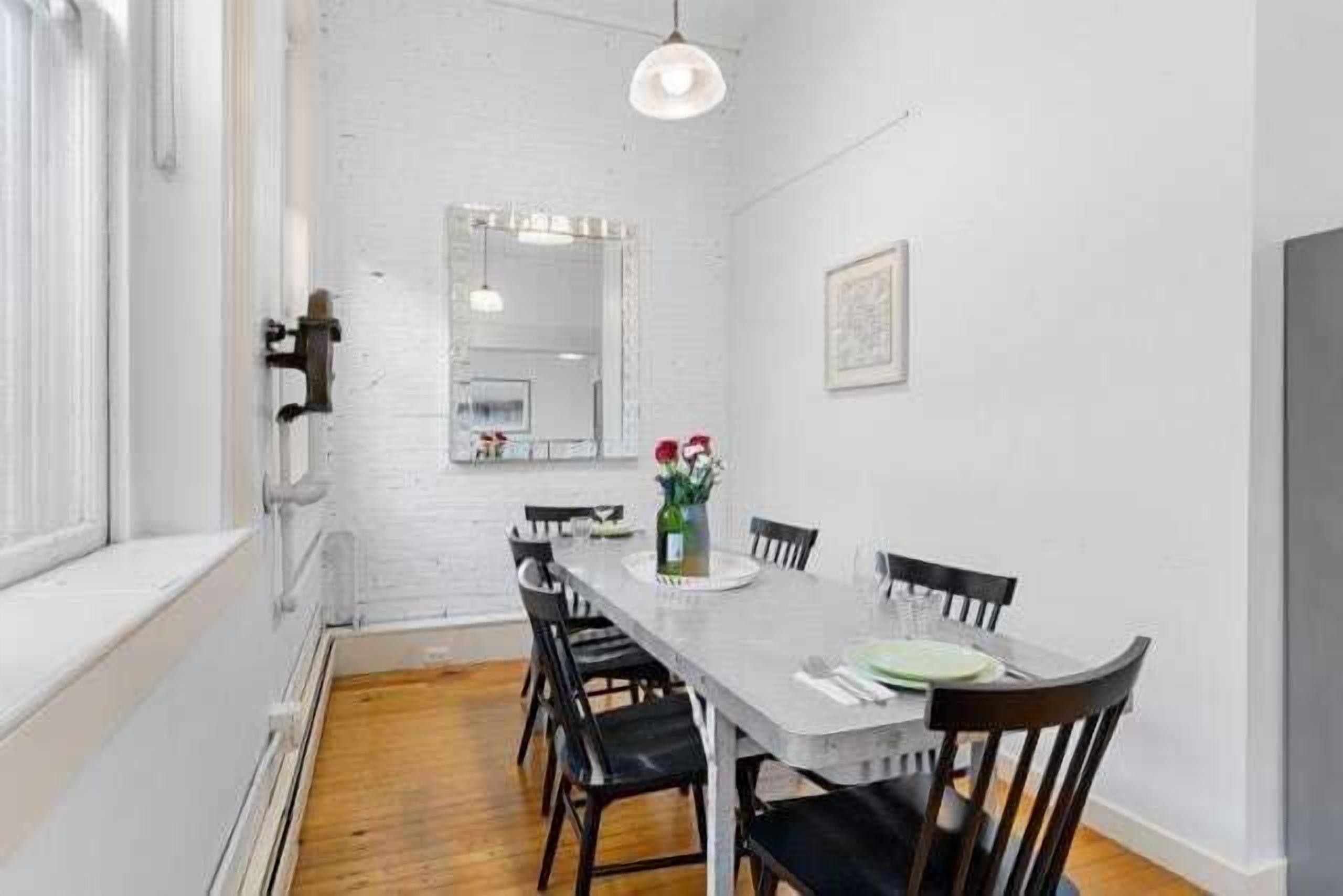 Un comedor con una mesa larga, sillas, una lámpara colgante, un espejo y un cuadro en la pared.