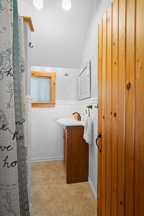 A bathroom with a wooden wardrobe, a white sink, a mirror, and a window. - Settlers Cottage, cute Maine home with water views (Cushing)