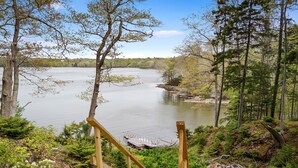 A wooden staircase leading to a dock by a calm lake surrounded by trees. - Settlers Cottage, cute Maine home with water views (Cushing)