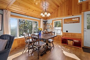 A wooden interior with a dining table, chairs, a bench, and large windows. - Settlers Cottage, cute Maine home with water views (Cushing)