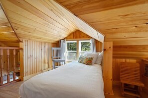 A wooden cabin bedroom with a bed, a window, and a chair. - Settlers Cottage, cute Maine home with water views (Cushing)