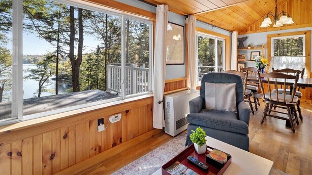 A cabin with large windows, a dining area, and a cozy seating area. - Settlers Cottage, cute Maine home with water views (Cushing)