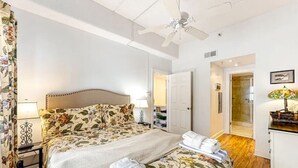 Een slaapkamer met een bed, nachtkastjes, een plafondventilator, een deur en een zichtbare badkamer door een open deur.