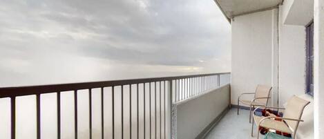 Ein Balkon mit Metallgeländer, zwei Stühle und einem kleinen Tisch.