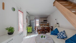 Een compact woongedeelte met een kitchenette, een eethoek en een bed met blauwe kussens.