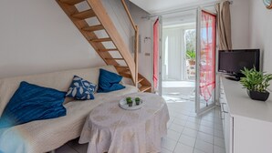 Een knus ingerichte kamer met een houten trap, een bank met blauwe kussens, een bijzettafeltje met een plant en een televisie op een wit kastje.