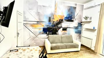 Un soggiorno moderno con un divano grigio, un grande quadro astratto e un televisore piatto montato a parete.