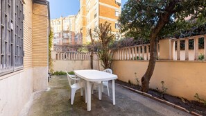 Un cortile con un tavolo e sedie bianche, circondato da edifici e un albero.