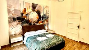 Una camera da letto con un letto, un comodino, una lampada, una porta e una parete con arte astratta.