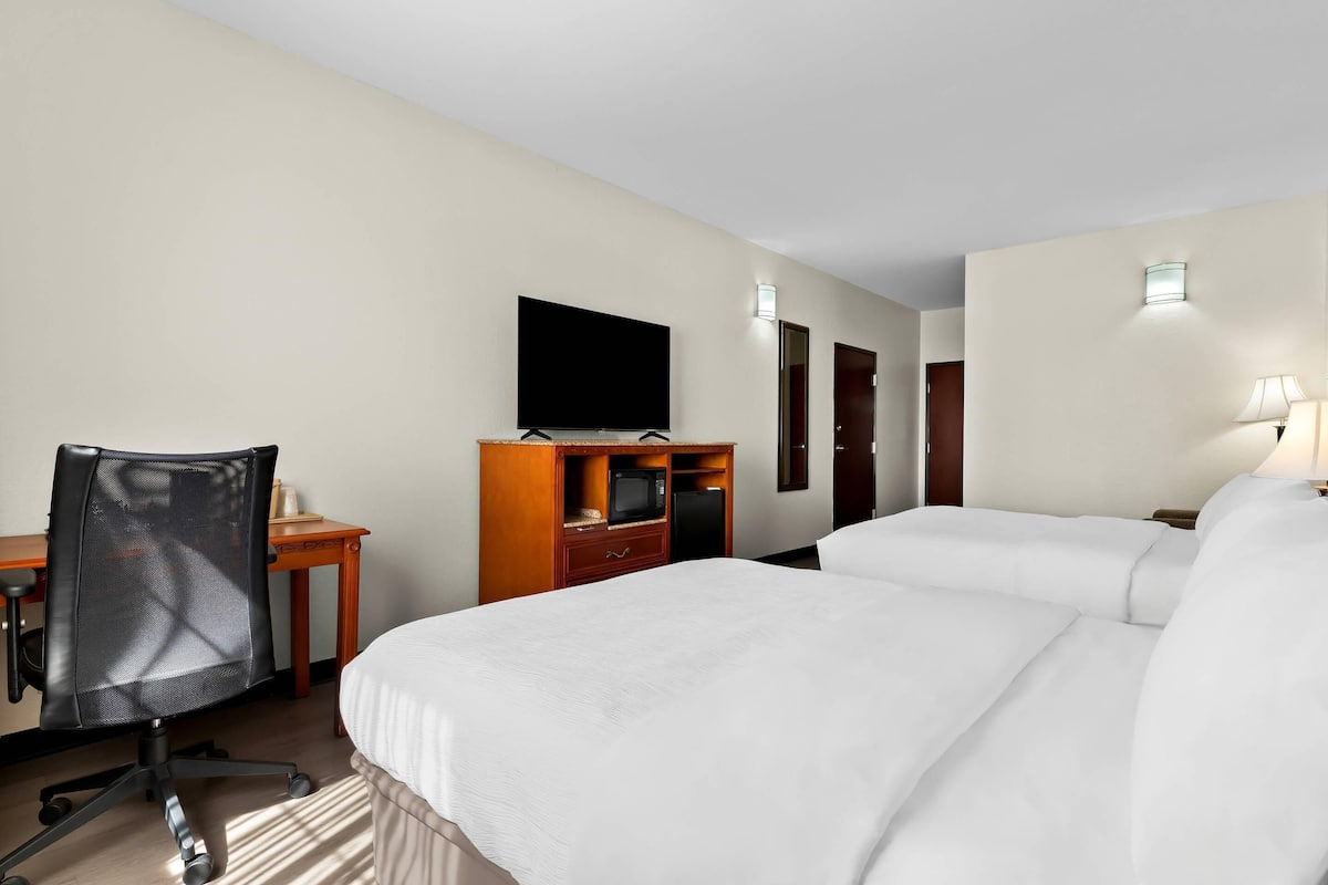 A hotel room with a large bed, a desk with a chair, a television, and a lamp.