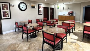 A hotel lobby with multiple round tables and red chairs, a clock on the wall, framed artwork, and a coffee station. - Quality Inn & Suites McAlester on Hwy 69 (McAlester)