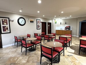 A hotel lobby with multiple round tables and red chairs, a clock on the wall, framed artwork, and a coffee station. - Quality Inn & Suites McAlester on Hwy 69 (McAlester)