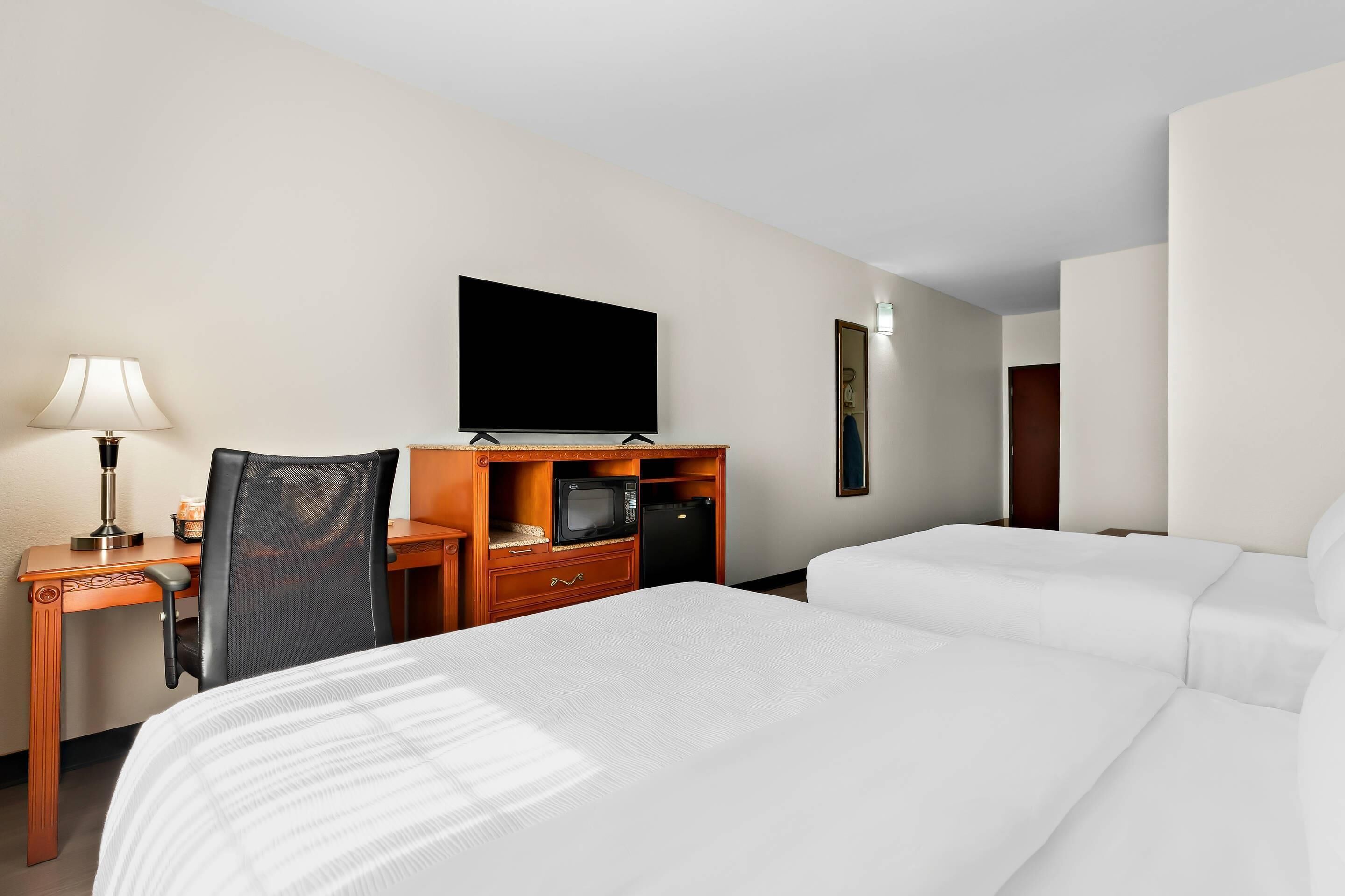 Una habitación de hotel con una cama, un escritorio con lámpara, un televisor y un microondas.
