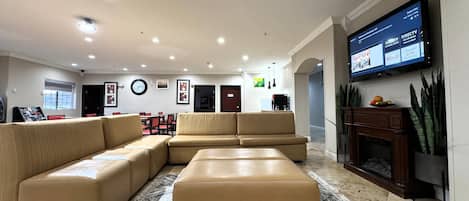 A spacious living room with a large sectional sofa, a flat-screen TV mounted on the wall, and a fireplace.